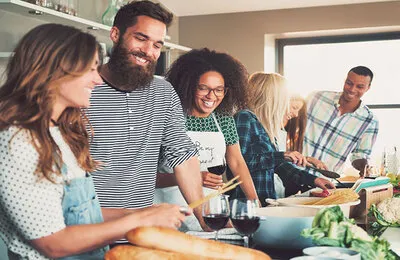 A diverse group of friends is happily cooking together in a bright kitchen, sharing a meal preparation.