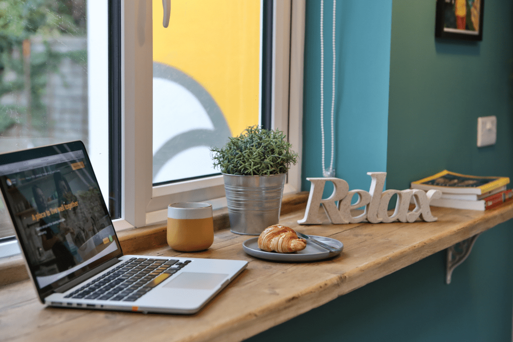 home breakfast station at a window, with an open laptop, a plant, a cup of coffee and a crossaint