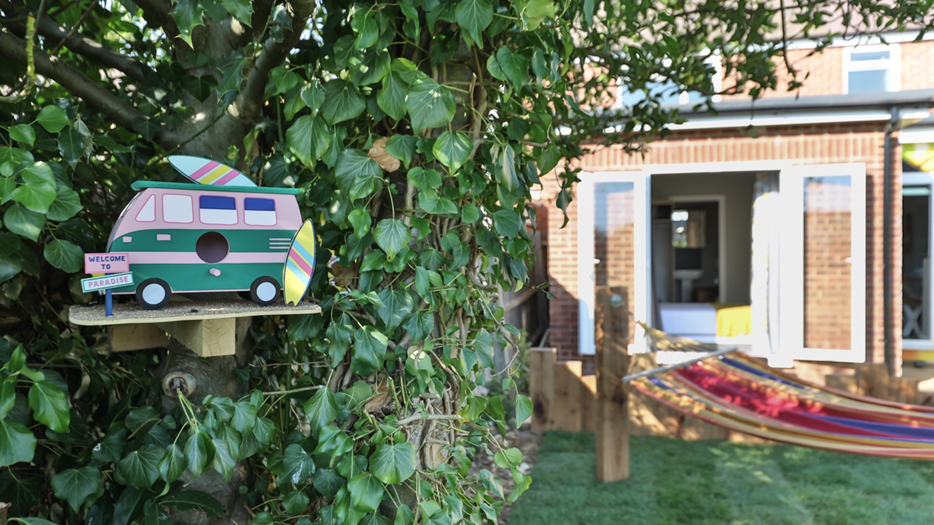 bhive-featured Coliving home, view from the garden, bird house with sign 'paradise' in front