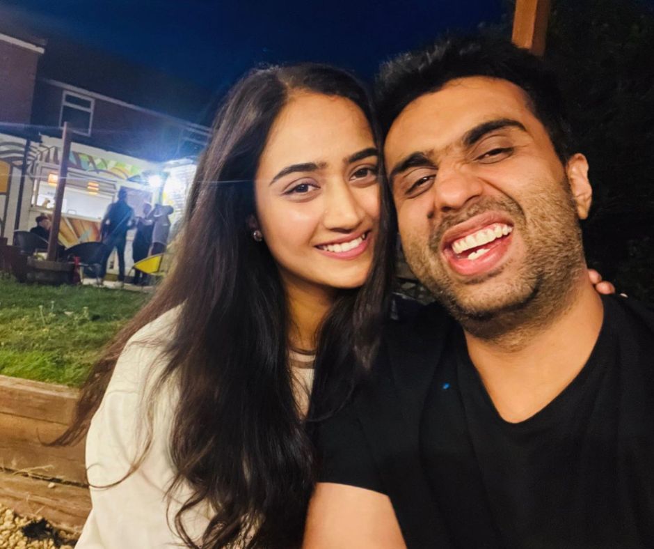 A happy couple is taking a selfie at night, with the man laughing and the woman smiling warmly.