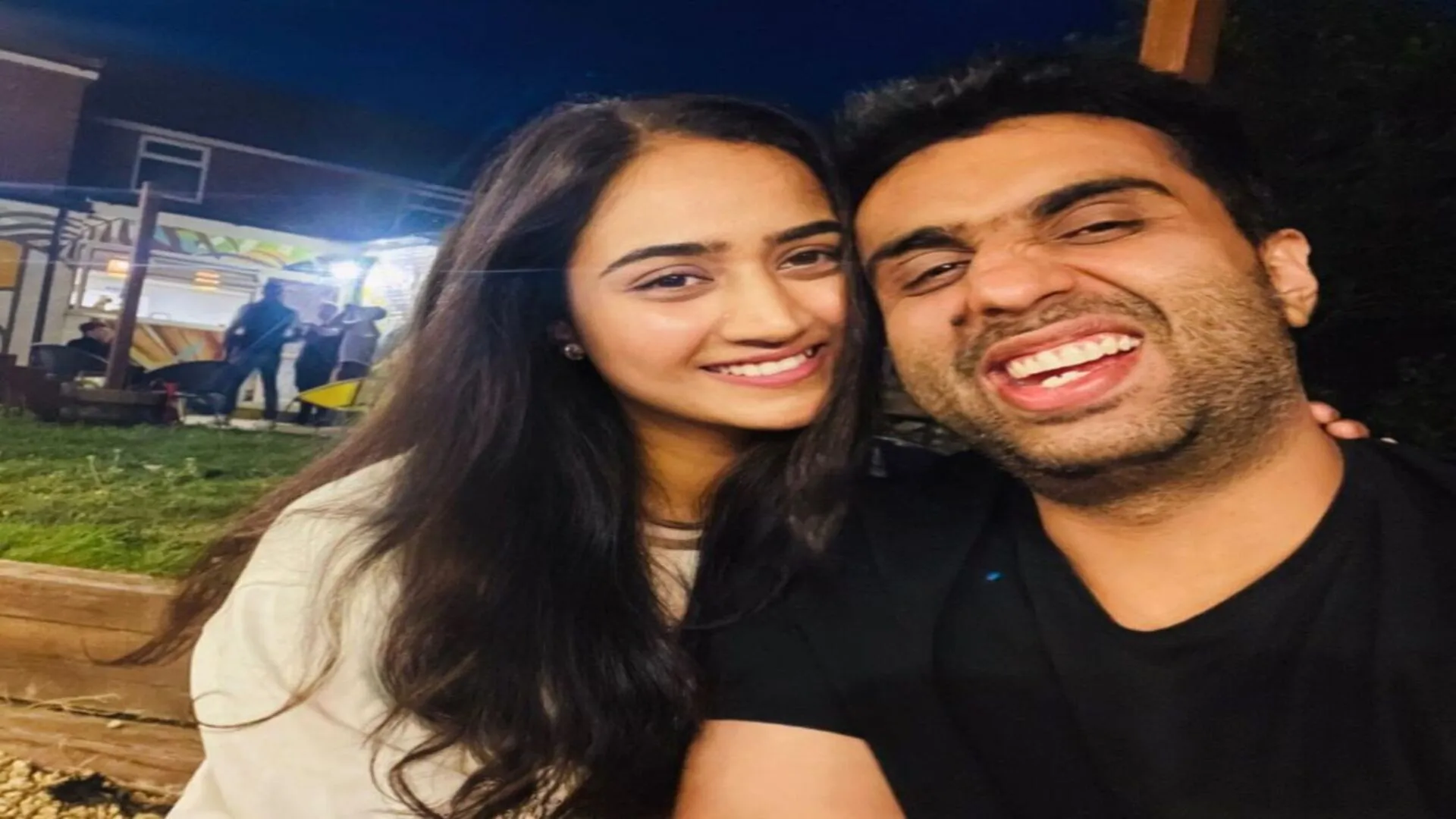 A happy couple is taking a selfie at night, with the man laughing and the woman smiling warmly.
